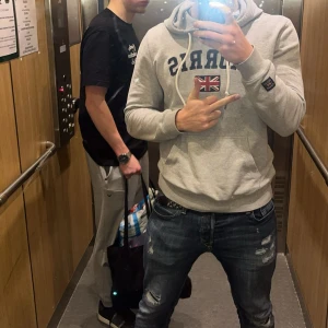 Grå hoodie från Morris  - Säljer en grå hoodie från Morris med svart text och brittisk flagga på bröstet. Tröjan har huva med vita snören och en stor magficka. Perfekt för chill dagar och snygg till jeans. Har en liten defekt vid ena snöret. Materialet är mjuk bomullsmix. Skit bra ny till hösten och passar till de flesta stilarna!!