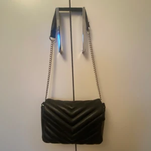 Svart quiltad axelväska med kedja - Snygg svart väska från klitter. Köpt för ca 300 spänn men säljer för 175kr. Man kan justera ifall man vill ha den som axel väska eller hand väska. Stängs med knapp och har innerficka med dragkedja. Nästan aldrig använd. Kontakta ifall du har frågor 🫰