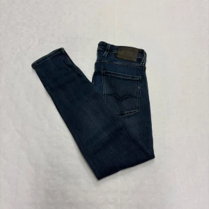 Blå Replay Anbass - Snygga mörkblå jeansbyxor från Replay med klassisk femficksdesign och diskreta sömmar på bakfickorna. Jeansen har rak passform och är tillverkade i mjukt denimtyg som ger en skön känsla. Perfekta för dig som gillar stilrena och tidlösa jeans.