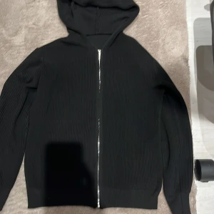 Svart ribbad hoodie med dragkedja - Svart hoodie från ”Axel Luxe” med ribbad struktur och hel dragkedja framtill. Tröjan har huva och långa ärmar, perfekt för en chill och stilren look. Materialet känns mjukt och följsamt, och den svarta färgen gör den enkel att matcha med allt. Storlek XXS men sitter som XS