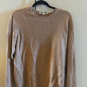 Beige kashmirtröja från Uniqlo - Mjuk och lyxig beige kashmirtröja från Uniqlo med rund halsringning och långa ärmar. Enkel och stilren design som är perfekt för lager-på-lager under kyliga dagar. Tröjan har ribbade muddar vid hals, ärmslut och nederkant. Viss slitage finns längs halslinningen därav ett lägre pris. I övrigt i fint skick utan noppor. 