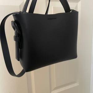 Svart axelväska från ARKET i skinn - Stilren svart axelväska från ARKET i slätt skinn. Väskan har knappt används, köpt för 1200kr. 18 cm i bredden 15cm i längden 