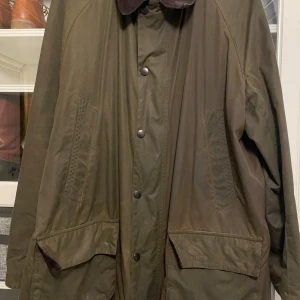 Olivgrön Barbour jacka med manchesterkrage - Använd fåtal gånger, inköpt för 4000kr.     Klassisk olivgrön oljerock från Barbour med brun manchesterkrage, stora fickor och dragkedja med knappar, Perfekt för höst och vinter, loose fit och långärmad modell.