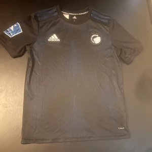 FC Köpenhamn fotbollströja - Snygg FC Köpenhamn matchtröja från Adidas i mörkblått och svart. Superliga märket på axeln är lite slitet men utöver det är tröjan i väldigt gott skick. Strl L i barnstorlek, passade mig när jag hade XS herr.