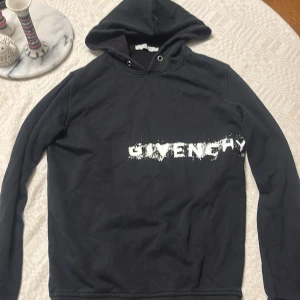 Svart Givenchy hoodie med tryck - L men passar M fint. Svart hoodie från Givenchy i 100% bomull med vit, sliten logotyp över bröstet. Klassisk huva med metallöljetter och långärmad modell. Perfekt för dig som gillar streetwear och exklusiva märken.