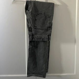 Grå jeans från Zara, storlek 34 - Säljer ett par grå lågmidjade jeans från Zara i storlek 34. Jeansen har raka ben, klassiska bakfickor och knäppning med knappar framtill. 