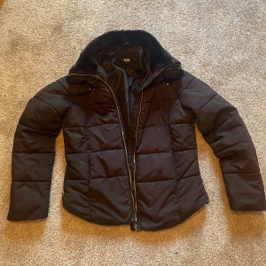 Svart pufferjacka med fuskpäls från bikbok - Svart pufferjacka från bikbok med snygg fuskpäls på kragen och guldiga dragkedjor. Jackan är quiltad och har lång ärm, perfekt för kalla dagar. Snygg passform och riktigt skön att bära under vintern.