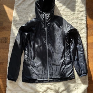 Mörkblå dunfri jacka från Houdini M - Blå , lätt och smidig jacka från Houdini i storlek M. Jackan är dunfri, har huva, hel dragkedja framtill och två sidofickor med dragkedja. Perfekt för kyliga dagar och enkel att packa ner i väskan. Snygg minimalistisk design med Houdini-logga på bröstet. Inga fläckar, allt funkar, inget trasig , spår av användning finns (se bild framsida, höger i nivå med fickan) Dock inget som syns om man inte granskar noga.