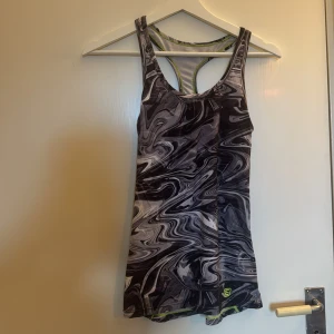 Energetics svartvit träningstopp - Sportig linnetopp från Energetics i svartvitt marmormönster med neongröna sömmar. Modellen är ärmlös med brottarrygg och tillverkad i funktionsmaterial som andas bra. 