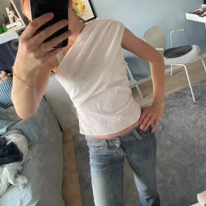 Vit oneshoulder topp i bomull - Säljer en vit oneshoulder topp i bomull med draperad framsida. Toppen är ärmlös på ena sidan och har en snygg asymmetrisk skärning som ger en cool och modern look. Perfekt att styla med jeans eller kjol för en trendig outfit. Från hm, säljer då jag har en nästan exakt likadan!