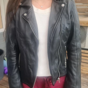 South Side Serpents skinnjacka från serien Riverdale  - Säljer en svart skinnjacka med coolt South Side Serpents-märke broderat på ryggen. Jackan har dragkedjor framtill och vid fickorna, klassisk bikerstil och snygga detaljer. Perfekt för dig som vill sticka ut och köra en edgy look.