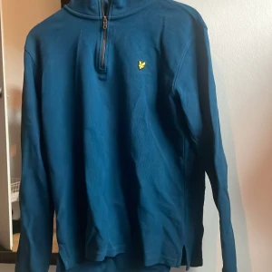 Blå half zip tröja från Lyle & Scott - Snygg blå långärmad tröja från Lyle & Scott med half zip och klassisk gul logga på bröstet. Tröjan har hög krage och är tillverkad i mjuk bomull, perfekt för en chill och stilren look. Kontakta mig om ni har några funderingar