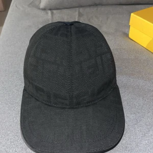 Svart Fendi keps  - Snygg svart keps från Fendi med diskret FF-logomönster över hela kepsen. Klassisk böjd skärm och justerbart spänne bak i läder. Tillverkad i ett tygmaterial med exklusiv känsla, perfekt för dig som gillar stilrena accessoarer.