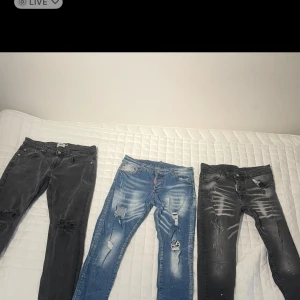 Tre par slitna jeans i olika färger - Tre par jeans med slitningar och hål, ett par i ljusblå denim och två par i svart/grå tvätt. Alla har skinny passform och tydliga slitdetaljer på benen för en trendig look. Perfekta för dig som gillar streetstyle och att sticka ut. Ni kan fråga privat om mer bilder och storlek på de i privat. 500 för alla de tre jeans 