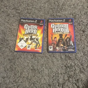 Guitar Hero World Tour & Guitar Hero III: Legends of Rock (PlayStation 2) - Två klassiska Guitar Hero-spel till PlayStation 2: World Tour och Legends of Rock. Båda med originalfodral, manualer och skivor i fint skick. Perfekt för musik- och partykvällar! Inga synliga repor eller skador.