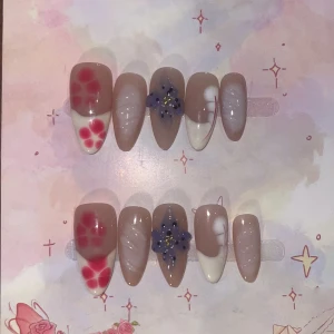 XS - Press on-naglar med blommor och mönster - Snygga press on-naglar i nude med röda och vita blommor, lila 3D-blomdetaljer och vita swirl-mönster. perfekt för dig som vill ha unika och kreativa naglar.                                                         💕OBS!💕 Dessa var en av de första jag gjorde så det avr lite skakigt med french tip på tummarna. Det är dock inte något mycket man lägger märke till!