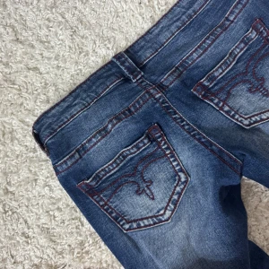 Blå bootcut jeans med röda sömmar - Snygga blå jeans från Gina tricot med bootcut passform och markerade röda sömmar. Jeansen har klassiska bakfickor med broderad detalj och normalhög midja. Tillverkade i stretchig denim för en bekväm känsla och snygg siluett. Storlek 170, passar xs/s