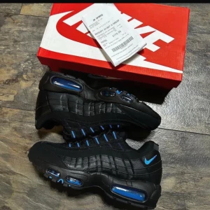 Nike Air Max 95 Svart/Blå Sneakers - Nike Air Max 95 sneakers i svart med blå detaljer och synliga Air-enheter. Skorna har en sportig design med snörning och rund tå. Tillverkade i syntet och skinn för en cool och modern look. Perfekta för dig som gillar streetwear och vill sticka ut.priset kan diskuteras privat 