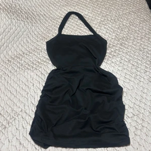 Svart kort halterneckklänning - Snygg svart kort klänning med halterneck och figurnära passform. Perfekt för dig som gillar en enkel men stilren look. Klänningen är ärmlös och har en klassisk siluett som passar till många tillfällen.