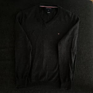 Svart v-ringad tröja Tommy Hilfiger - Klassisk svart v-ringad tröja från Tommy Hilfiger med diskret logga på bröstet. Tröjan har långa ärmar och ribbade muddar vid ärmslut och nederkant. Perfekt för en stilren och enkel look.