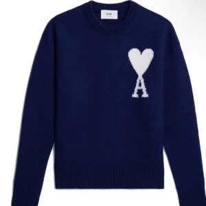 Mörkblå stickad tröja från Ami - Säljer en mörkblå stickad tröja från Ami med ett stort vitt hjärta och bokstaven A på bröstet. Tröjan har rund hals, ribbade muddar och lång ärm. Perfekt för dig som gillar stilrena plagg med en twist.