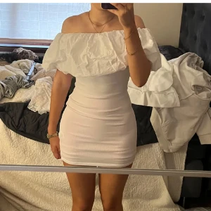 Vit offshoulder kortklänning Zara - Superfin vit kortklänning från Zara med offshoulder och stor volang upptill. Klänningen är tight och har en figurnära passform. Perfekt för dig som vill sticka ut med en trendig och stilren look. Materialet känns mjukt och stretchigt.