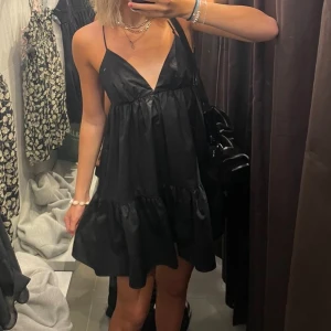 Svart kort klänning med tunna axelband - Supersöt svart kort klänning från bikbok med tunna axelband och v-ringning. Klänningen har en luftig passform, volangkant nertill och snygg snörning i ryggen. Perfekt för varma dagar och enkel att styla med smycken eller en cool väska.