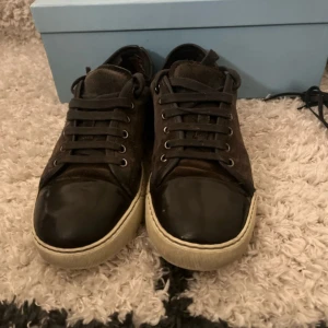 Svarta sneakers från Lanvin i mocka - Snygga svarta sneakers från Lanvin med ovandel i mocka och tåparti i blankt skinn. Skorna har vita sulor och klassisk snörning. Kommer med originalkartong och dustbags. Perfekta för dig som gillar stilrena och exklusiva sneakers.