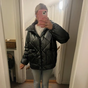 Mohito Jacka - Säljer en svart pufferjacka med quiltat mönster och stor huva. Jackan har dragkedja framtill, två stora fickor och en oversized passform. Perfekt för kalla dagar när du vill vara både varm och snygg.