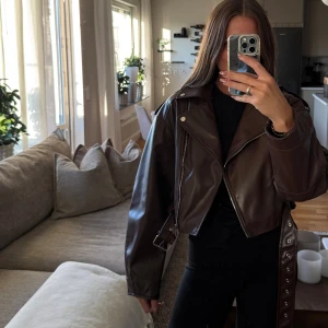 Brun skinnjacka  - Snygg brun skinnjacka från SHEIN i croppad modell med bälte och silvriga detaljer. Jackan har klassisk bikerstil med dragkedja, bred krage och långa ärmar. 