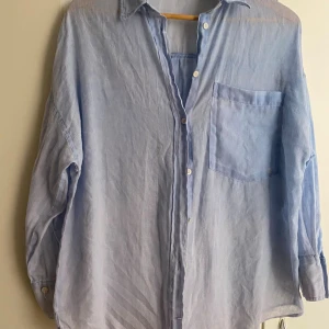 Ljusblå linneskjorta från Zara - Säljer en ljusblå skjorta från Zara i luftig linne. Skjortan har klassisk krage, bröstficka och knäppning framtill. Perfekt för en chill och stilren look. Passar dig som gillar en lite loose fit. 