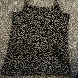 Leopardmönstrad linne från Lindex - Säljer ett snyggt leopardmönstrat linne från Lindex i storlek 158/164. Linnet har tunna axelband och är i beige och svart, perfekt för dig som vill sticka ut lite extra. Superenkel att matcha med jeans eller kjol.