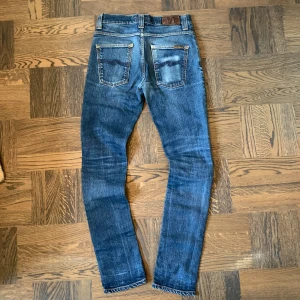 Blå jeans från Nudie Jeans GRIM TIM - Säljer ett par riktigt feta blå jeans från Nudie Jeans, GRIM TIM, med klassisk femficksdesign och snygg selvedge tvätt. W30 L34. Jeansen har pytte lite defekt vid skrevet (jättelitet hål) men inget man lägger märke till. Overall riktigt feta jeans med snygga slitningar! Vid frågor eller funderingar är det bara att fråga på! 