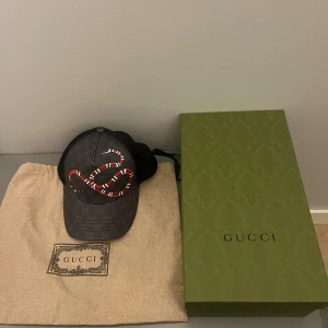 Gucci keps orm - Snygg svart keps från Gucci med klassiskt GG-mönster och en stor röd och vit orm på framsidan. Kepsen har böjd skärm och mesh på sidorna för extra ventilation. Kommer med original dustbag och grön Gucci-box. Perfekt för dig som gillar lyxiga detaljer.
