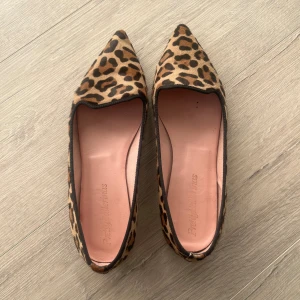 Leopardmönstrade ballerinaskor Pretty Ballerinas - Snygga ballerinaskor från Pretty Ballerinas i leopardmönstrad mocka med spetsig tå. Skorna har en beige och brun färgskala med svarta detaljer runt kanten och platt sula.