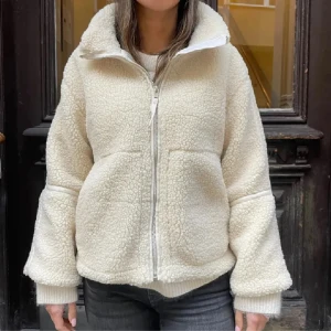 Vit teddyjacka med dragkedja - Mysig vit teddyjacka med hög krage och dragkedja framtill. Jackan har två stora fickor och är tillverkad i fluffigt teddy-material som håller dig varm. Perfekt för kyliga dagar och har en avslappnad, loose passform med långa ärmar. Bilderna är lånade men kan absolut skicka egna bilder ifall ni vill ha det! Det märks lite vid dragkedjan att den har används men det inte inget man ser! Kolla bild 4