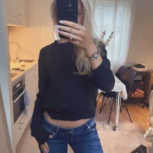 Svart  sweatshirt - En svart sweatshirt med rund hals och långa ärmar. Tröjan har ribbade muddar vid ärmslut och nederkant, vilket ger en snygg och avslappnad look. Perfekt till jeans för en enkel och stilren outfit.
