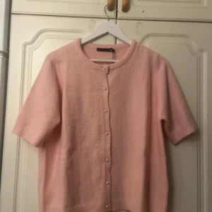 Kofta - Supersöt ljusrosa kofta från 157 med korta ärmar och pärlknappar framtill. Koftan är stickad och har en rund halsringning. Perfekt för lager-på-lager och ger en mjuk, feminin vibe till din outfit.