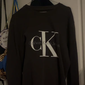 Svart Calvin Klein tröja XS - Svart långärmad tröja från Calvin Klein Jeans i storlek XS. Tröjan har en stor vit CK-logga framtill och är i mjukt bomullsmaterial. Enkel och stilren design med rund hals och ribbade muddar vid ärmslut och nederkant.