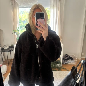 Svart teddyjacka med dragkedja - Mysig svart teddyjacka med hög krage och hel dragkedja framtill. Jackan har en loose passform och är tillverkad i fluffigt fleece-material som håller dig varm. Perfekt för kyliga dagar och enkel att styla till olika outfits. Köpt för 600 förra våren, inga tecken på användning, säljer då jag har för många jackor 💕