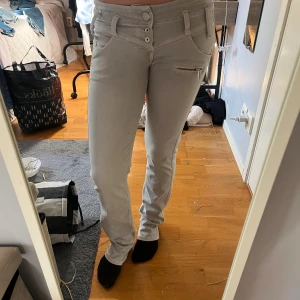 Gråa byxor Freeman T. Porter S - Snygga gråa byxor från Freeman T. Porter i storlek S. Byxorna har flera knappar i midjan, dragkedjedetaljer på fickorna och raka ben. Perfekt för dig som gillar en stilren look med coola detaljer.