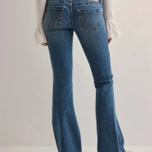 True Religion blå bootcut jeans - Säljer ett par blå jeans från True Religion med klassiska kontrastsömmar och tydliga bakfickor med logotypbrodyr. Modellen har bootcut-ben och väldigt låg midja, tillverkade i mjukt denimtyg. Perfekta för dig som gillar en retroinspirerad look.ORDINARIE PRIS 1400