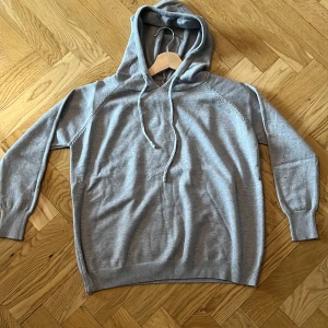 Ljusgrå hoodie med huva och snörning - Säljer en stilren ljusgrå hoodie med huva och snörning. Tröjan har långa ärmar, ribbade muddar och en avslappnad passform. Perfekt för chill dagar eller när du vill ha något bekvämt och enkelt.