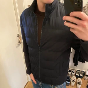 Mörkblå Cardigan  - Stilren marinblå cardigan från Zara i storlek M. Jackan har hög krage, raka ärmar och dragkedja framtill. Lätt vadderad med diskreta fickor på sidorna. Perfekt för kyliga dagar och enkel att matcha med jeans eller hoodies.