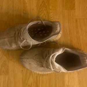 Beige adidas Yeezy Boost 350 sneakers - Säljer ett par beige adidas Yeezy Boost 350 sneakers med stickad ovandel och klassisk snörning. Skorna har en rund tå och platt sula i gummi för skön komfort. Perfekta för dig som gillar streetwear och vill ha något stilrent men ändå unikt.