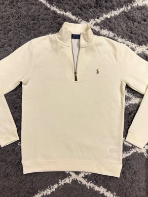 Polo Ralph Lauren half zip - Snygg vit långärmad tröja från Polo Ralph Lauren med klassisk ståkrage och half zip-dragkedja framtill. Tröjan har det ikoniska Polo-logot broderat på bröstet och är gjord i mjuk bomull. Storlek S. Jag är 180cm och den passar mig perfekt.