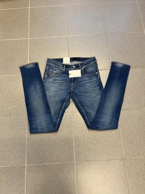 Blå slimmad jeans från tiger of sweden W29 L32 - Snygga blå jeans med slim passform och smal fot. Klassisk femficksmodell med orangea sömmar och lätt slitning på låren. Perfekta för dig som gillar en smal siluett och vill ha ett par stilrena jeans till vardags. 