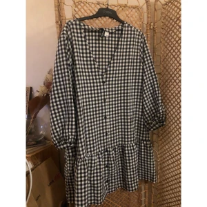 Rutig kortklänning från H&M Divided - Supersöt svartvit rutig kortklänning från H&M Divided. Klänningen har v-ringning, knappar framtill och trekvartsärmar med resår. Den har en avslappnad passform och volang nedtill, perfekt för en chill och trendig look.