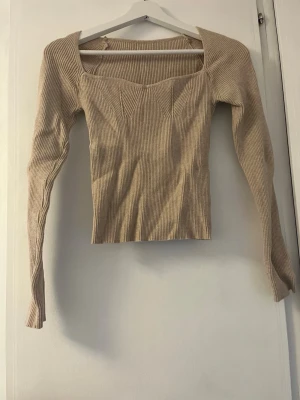 Beige ribbad långärmad topp - Säljer en beige ribbad topp med lång ärm och snygg fyrkantig halsringning. Toppen har markerade sömmar framtill som ger en cool form och sitter figurnära. Perfekt att styla med jeans eller kjol för en trendig look.