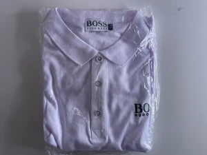 Vit polotopp från Hugo Boss XL - Säljer en fräsch vit polotopp från Hugo Boss i storlek XL. Toppen har klassisk krage, tre knappar framtill och broderad logga på bröstet. Perfekt för dig som gillar stilrena och enkla plagg med snygg passform. Finns i flera storlekar. Från M till XL